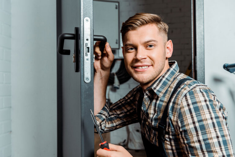 Cheerful locksmith holding a screwdriver while working on a door lock, illustrating mobile locksmith services for vehicle entry and key replacement.