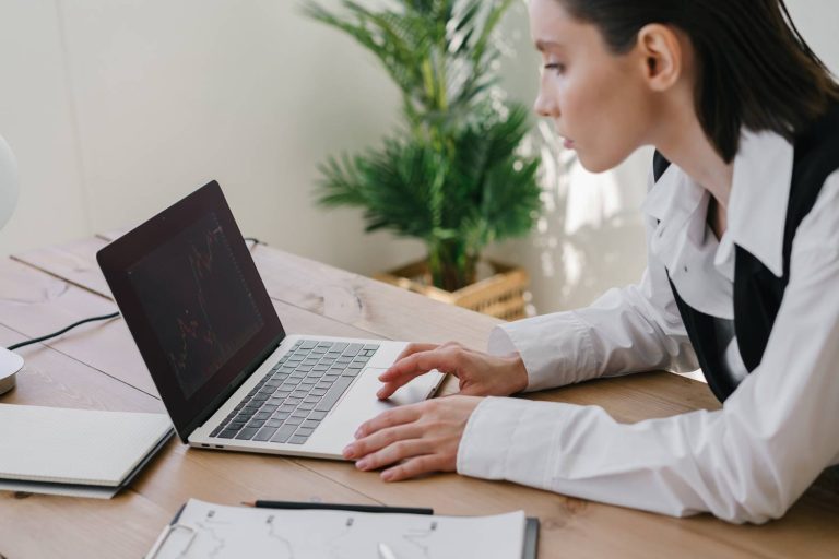 Woman working on laptop in modern office, analysing data and charts, surrounded by greenery, showcasing digital marketing and website development expertise.