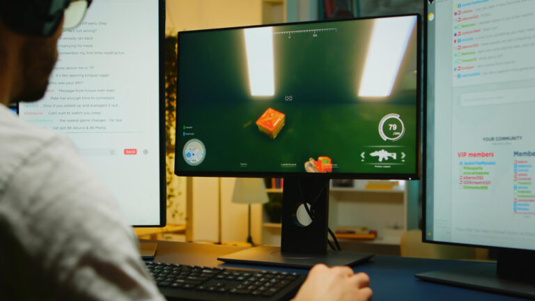 Person gaming on a dual-monitor setup, displaying a video game interface with a highlighted item and chat window, illustrating digital engagement and technology in modern entertainment.